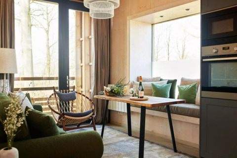 Moderne tiny house stue i The Lodge by YourNature, Belgien, med grøn sofa, spisebord og store vinduer.