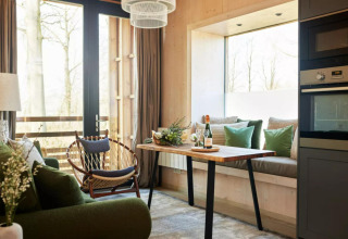 Moderne tiny house stue i The Lodge by YourNature, Belgien, med grøn sofa, spisebord og store vinduer.