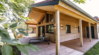 Buitenaanzicht van Chalet Bungalow met houten bekleding, overdekt terras en ligzetels in groene natuur.