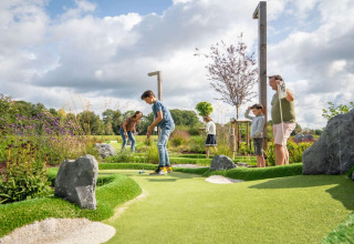 Familie spielt gemeinsam Minigolf auf einer gepflegten Outdoor-Anlage bei einem Glamping-Resort.