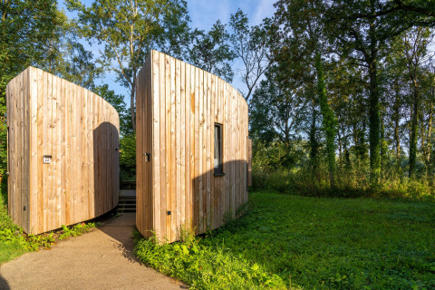 Moderne Holzhütte namens ‚The Lodge by YourNature‘ in Belgien, eingebettet in eine grüne Naturlandschaft.