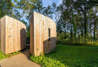 Moderne Holzhütte namens ‚The Lodge by YourNature‘ in Belgien, eingebettet in eine grüne Naturlandschaft.