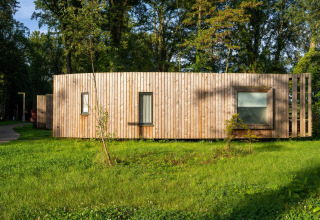 Moderne tiny house kaldet The Lodge af YourNature, omgivet af grønt græs og høje træer i dagslys.