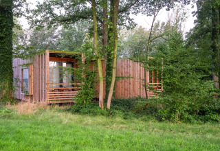 Eine moderne Holzhütte inmitten eines bewaldeten Gebiets in Belgien, teilweise von Bäumen verdeckt.