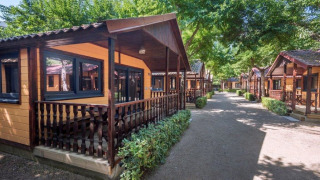 Rij houten chalets met veranda’s en groene omgeving bij Camping Solmar - XALET op een zonnige dag.