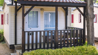 Stacaravan bij Camping Solmar, COTTAGE B, met houten terras, picknickbank en groene haag vooraan.