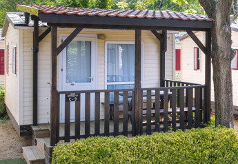 Casa mobile al Camping Solmar, COTTAGE B, con veranda in legno, panche esterne e siepe verde davanti.