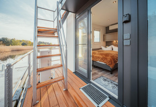 Vista della terrazza e della camera da letto della houseboat 'am Gräbendorfer See' in Germania, con scala in legno.