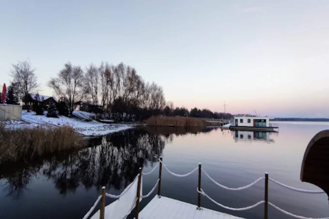 Vista del Houseboat «am Gräbendorfer See» sobre un lago tranquilo con orillas nevadas y reflejos, en Alemania.