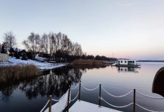 Scenic view of Houseboat 'am Gräbendorfer See' on a calm lake with snowy banks and gentle reflections, Germany.