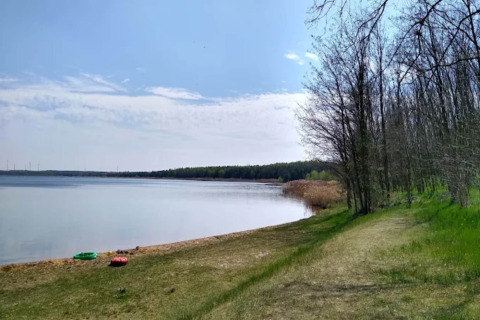 Peaceful lakeshore with grassy area, trees, and kayaks by Houseboat am Gräbendorfer See in Germany.