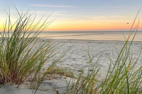 Sunset view from the sandy beach with grass in front of Houseboat «in Peenemünde» in Germany.