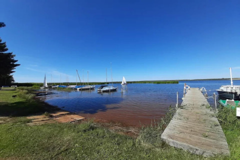 Casa flotante junto a un lago con muelle de madera y veleros en Houseboat «am Gräbendorfer See», Alemania.