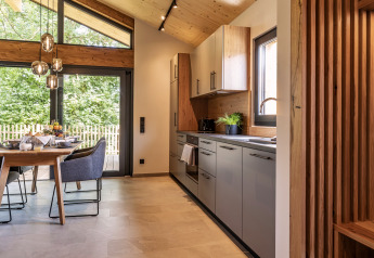 Cucina e zona pranzo di chalet moderno con ampie finestre, soffitto in legno e vista sul bosco in Germania.