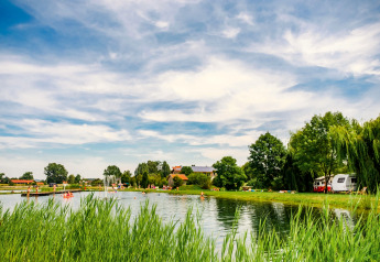 Scenario verdeggiante con lago, roulotte e persone al Chalet «Bungalow» in Germania sotto cielo nuvoloso.