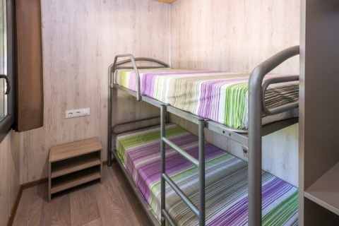 Stanza in una casa mobile al Camping Solmar in Spagna con letti a castello e biancheria a righe colorate.
