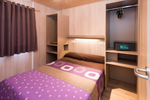Camera da letto in casa mobile con letto matrimoniale, armadio, cassaforte e tende marroni al Camping Solmar, Spagna.
