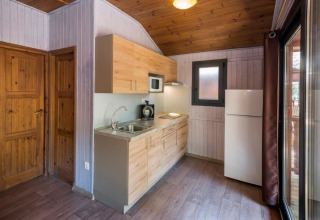 Moderne hyttekøkken på Camping Solmar - XALET i Spanien, med træloft, køleskab og vindue.