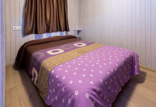 Chambre confortable d'un chalet au Camping Solmar en Espagne, avec couverture violette et murs en bois.