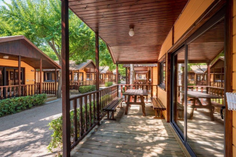 Chalets en bois avec terrasses et bancs au Camping Solmar - XALET en Espagne, ambiance ensoleillée.