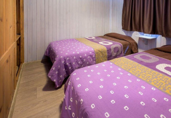 Et enkelt værelse i Camping Solmar - XALET i Spanien med to enkeltsenge og lilla sengetøj.