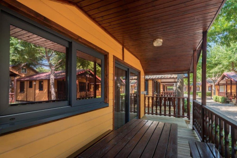 Véranda en bois et entrée du lodge Camping Solmar - XALET en Espagne, entouré d'autres chalets.