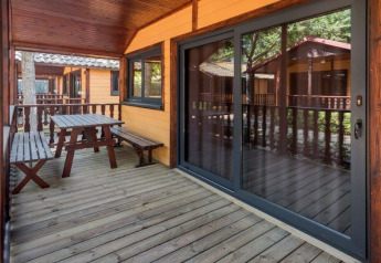 Træveranda med bænk og bord på Camping Solmar - XALET i Spanien, omgivet af træbeklædte hytter.