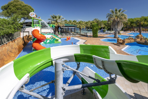 Vandland med rutsjebaner og swimmingpools på glampingplads under palmer og blå himmel.