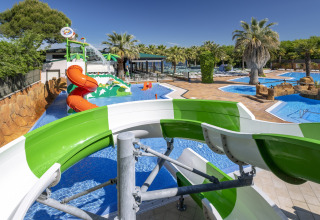 Vandland med rutsjebaner og swimmingpools på glampingplads under palmer og blå himmel.