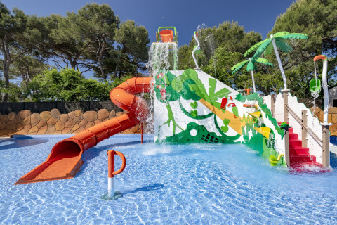 Aire de jeux aquatique avec toboggan, seaux et palmiers au Camping Solmar - XALET en Espagne.