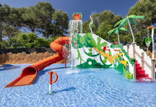 Parco giochi acquatico presso una casa mobile con scivoli colorati, secchi d’acqua e palme finte.