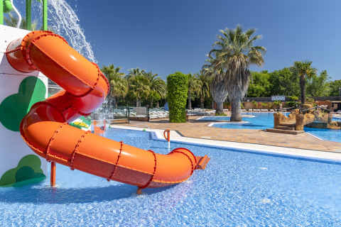 Kleurrijke waterglijbaan en kinderbad bij een glamping, omringd door palmbomen en helderblauw water.