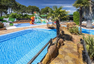 Piscina all'aperto in una struttura glamping con scivoli d'acqua, palme, vialetti in pietra e area bimbi.