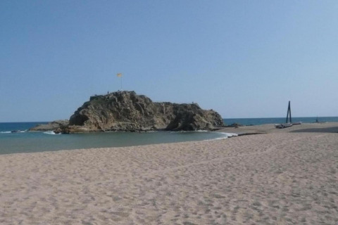 Photo d’une plage de sable avec une île rocheuse et ciel bleu, prise dans un hébergement glamping en bord de mer.