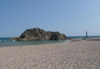 Foto di una spiaggia sabbiosa con isola rocciosa e cielo azzurro, scattata presso un alloggio glamping.