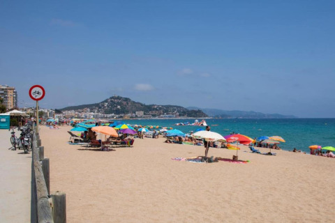 Spiaggia con ombrelloni colorati, bagnanti e colline costiere presso una struttura di glamping.