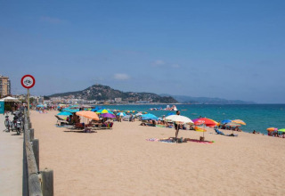 Spiaggia con ombrelloni colorati, bagnanti e colline costiere presso una struttura di glamping.