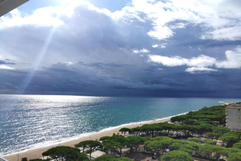Udsigt over Camping Solmar - XALET i Spanien, med strand, hav og træer under dramatiske skyer.