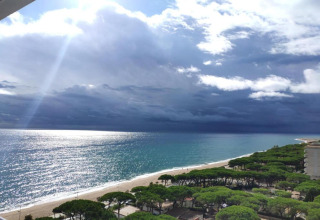 Vue depuis Camping Solmar - XALET en Espagne, plage, mer bleue, arbres et ciel nuageux impressionnant.