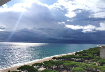 Udsigt over Camping Solmar - XALET i Spanien, med strand, hav og træer under dramatiske skyer.