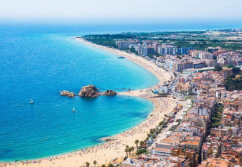 Luftfoto af strand og by nær Camping Solmar - XALET i Spanien, med klart blåt hav og mange bygninger.