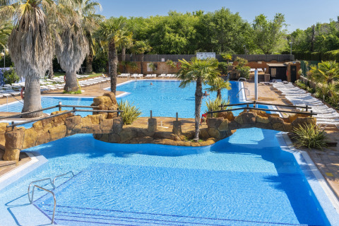 Ruim buitenzwembad met palmbomen en stenen brug bij Camping Solmar - COTTAGE B in Spanje.