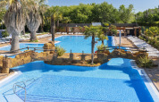 Ampia piscina all’aperto con palme e ponte in pietra al Camping Solmar - COTTAGE B in Spagna.