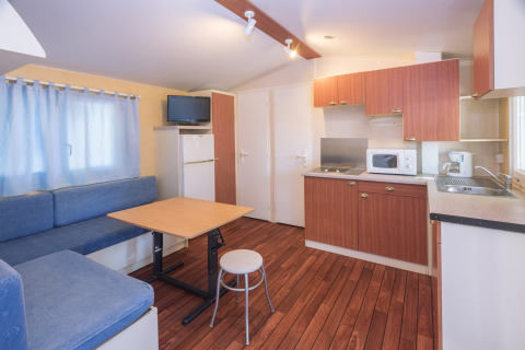 Interiør af mobilhome Camping Solmar - COTTAGE B med køkken, spiseplads og sofa i Spanien.