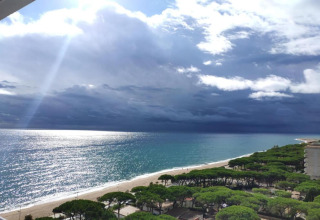 Zicht op het strand, de zee, zonnestralen, wolken en bomen bij Camping Solmar - XALET CONFORT in Spanje.