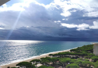 Zicht op het strand, de zee, zonnestralen, wolken en bomen bij Camping Solmar - XALET CONFORT in Spanje.