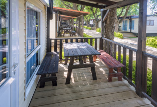 Træterrasse med borde og bænke foran mobilhomes i Camping Solmar - COTTAGE B, Spanien.