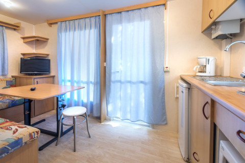 Lyst interiør i mobilhome på Camping Solmar - COTTAGE B, Spanien, med køkken, bord og tv.