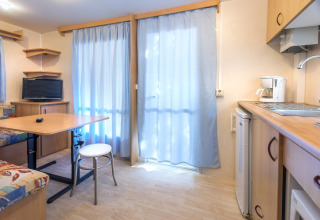 Lyst interiør i mobilhome på Camping Solmar - COTTAGE B, Spanien, med køkken, bord og tv.