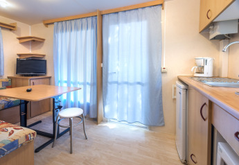 Interno luminoso di casa mobile al Camping Solmar - COTTAGE B, Spagna, con cucina, tavolo e TV.
